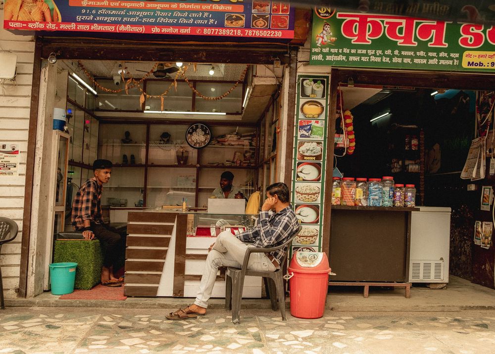 Local shops and storefronts with signage in Hindi script along a street in India.