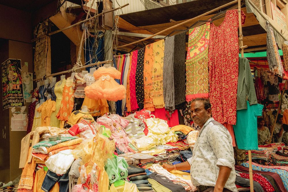 Colorful textiles and clothing hanging at market stalls along a busy street.