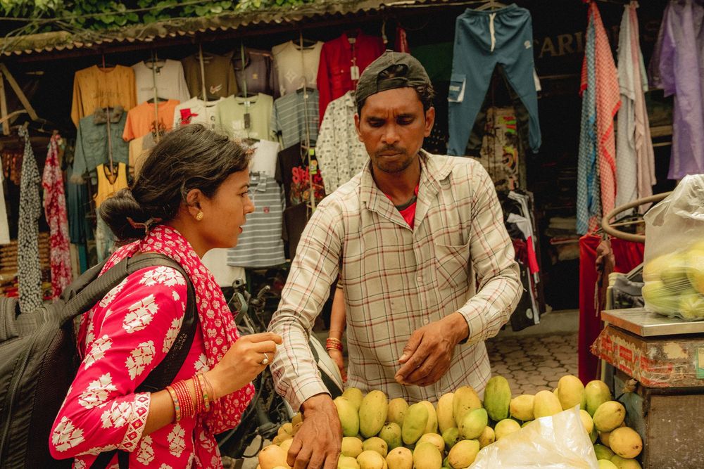 Market vendors selling fresh fruits and vegetables at outdoor stalls.