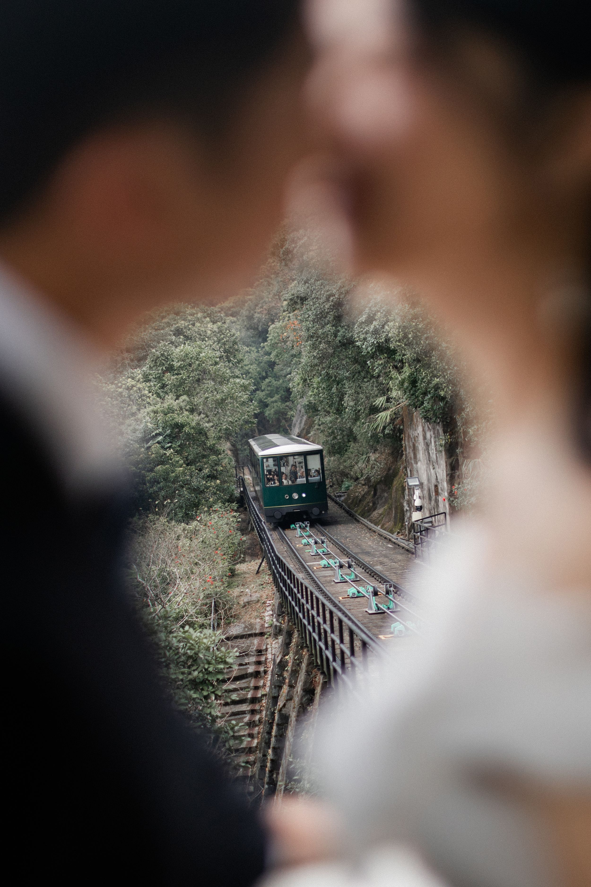 Blurred couple frames a vintage funicular tram descending through lush green hillside tracks.