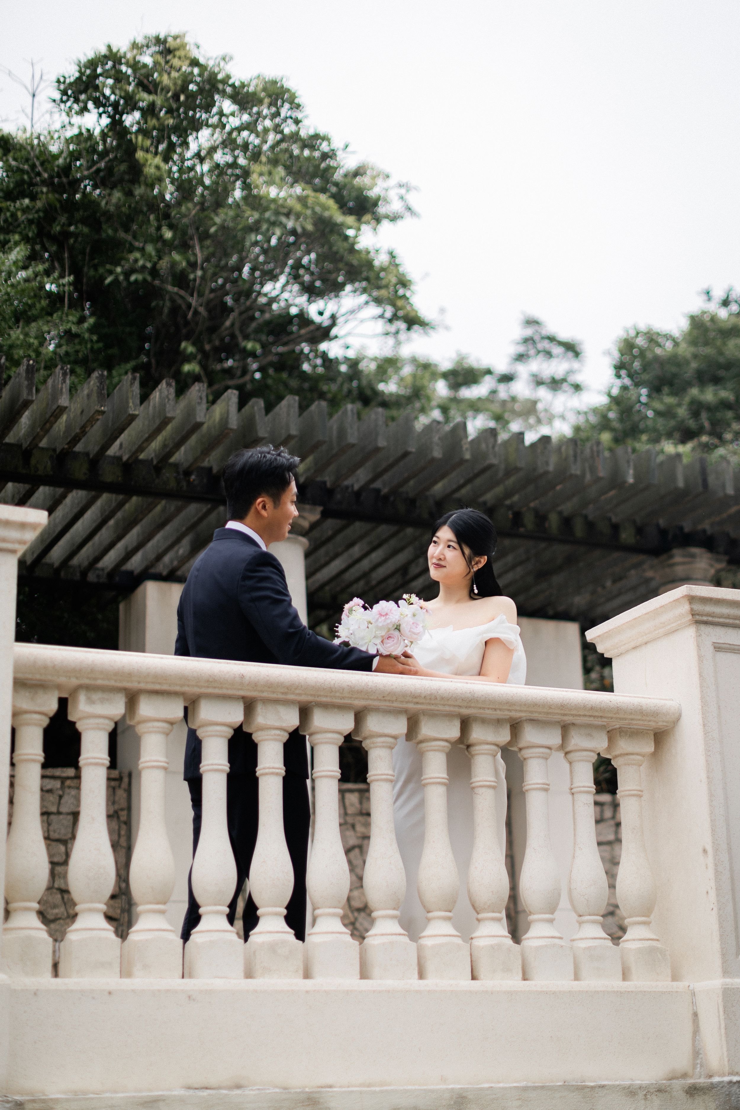 Bride and groom sharing a romantic moment at a white balustrade terrace surrounded by lush greenery.