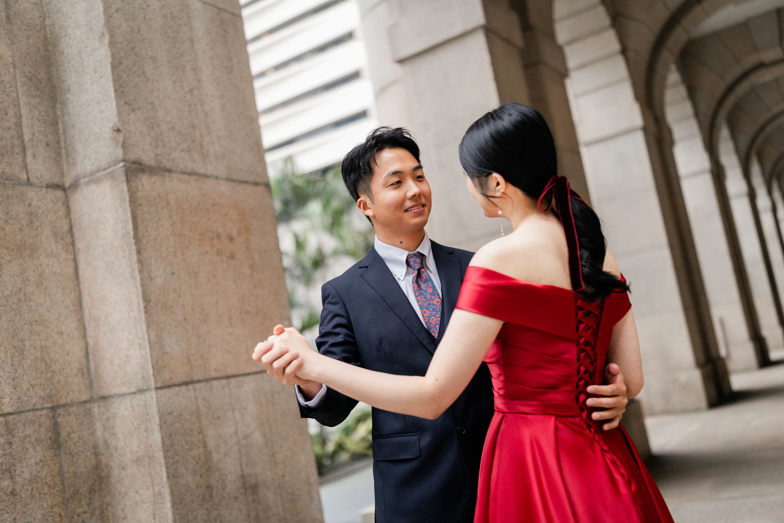 Couple shares a tender dance moment between stone columns, bride in elegant red dress.