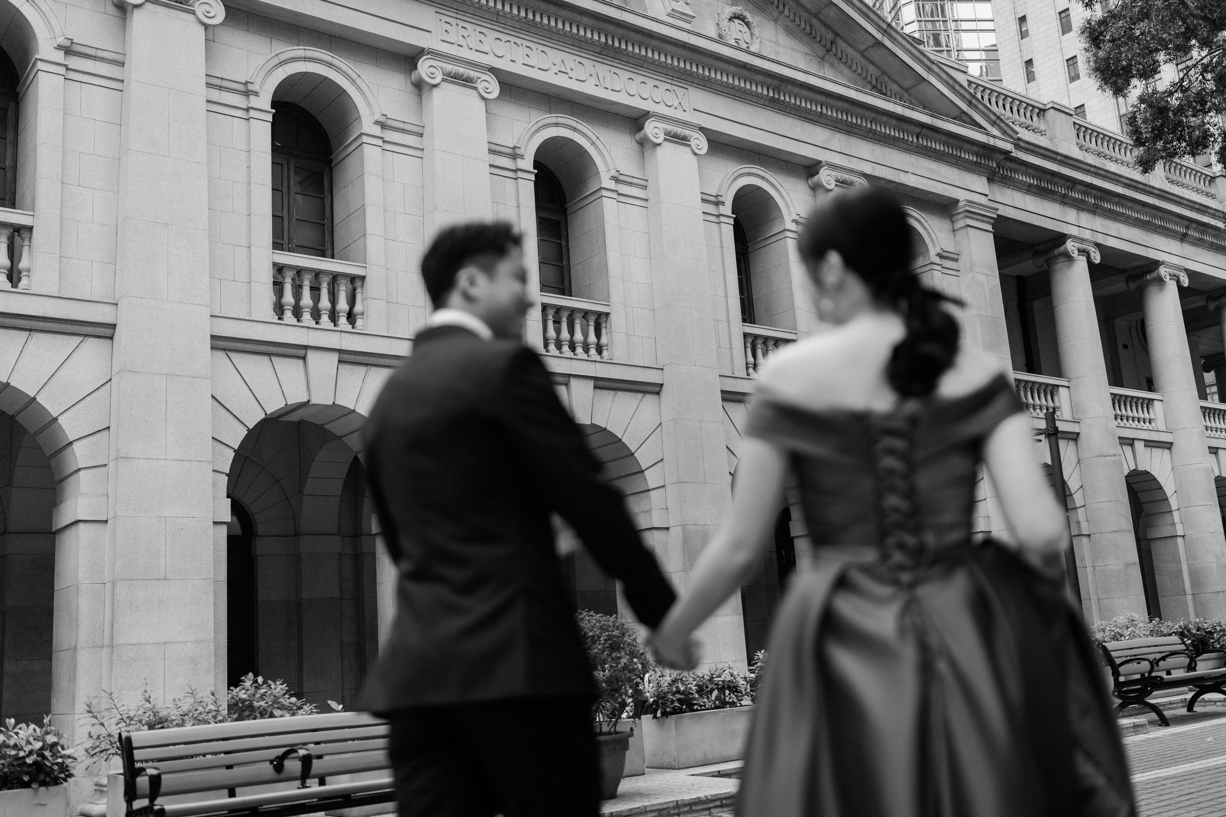 Black and white photo of couple walking hand in hand toward a grand colonial building.