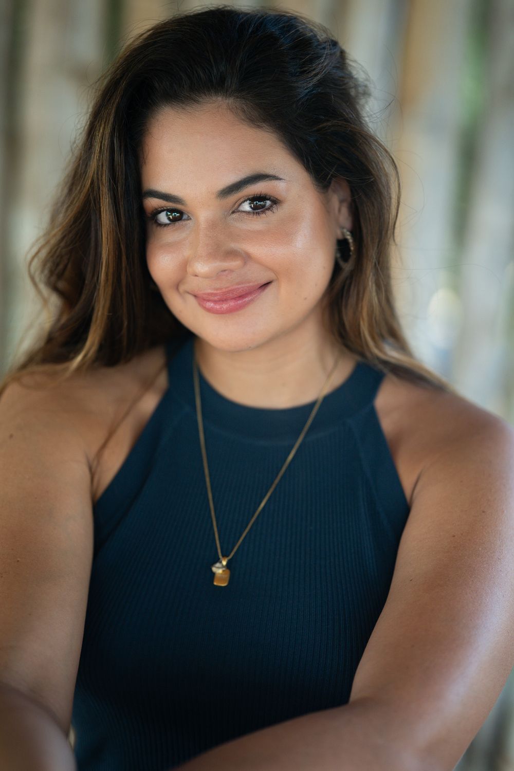 Portrait of someone wearing a navy blue sleeveless top and small pendant necklace, with flowing ombre hair and warm smile.