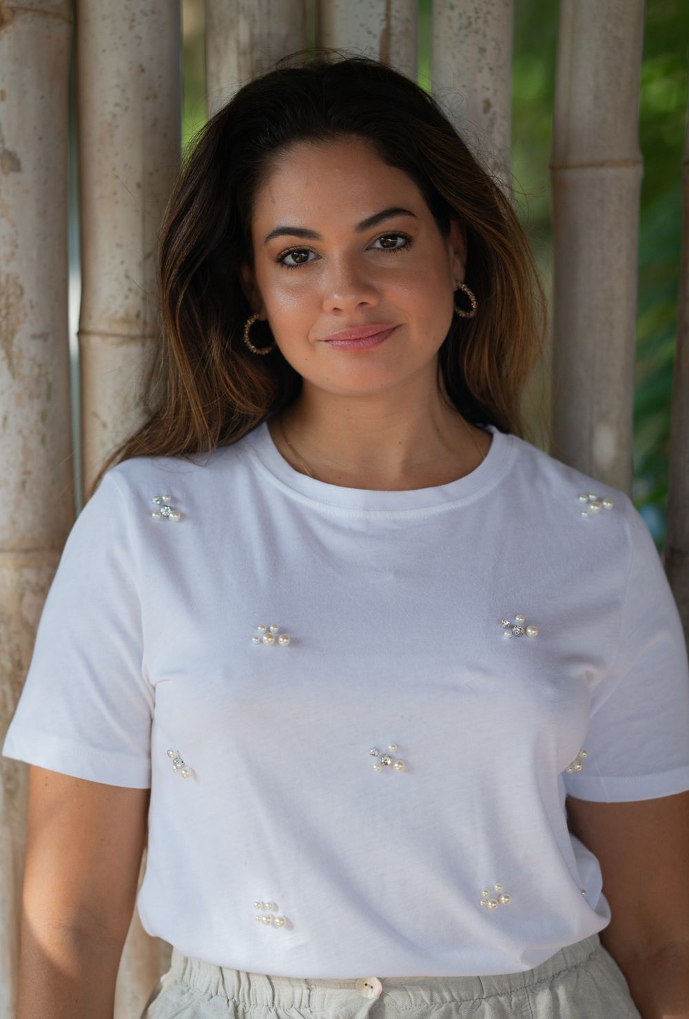 Smiling person in white t-shirt with floral embellishments against bamboo wall background.