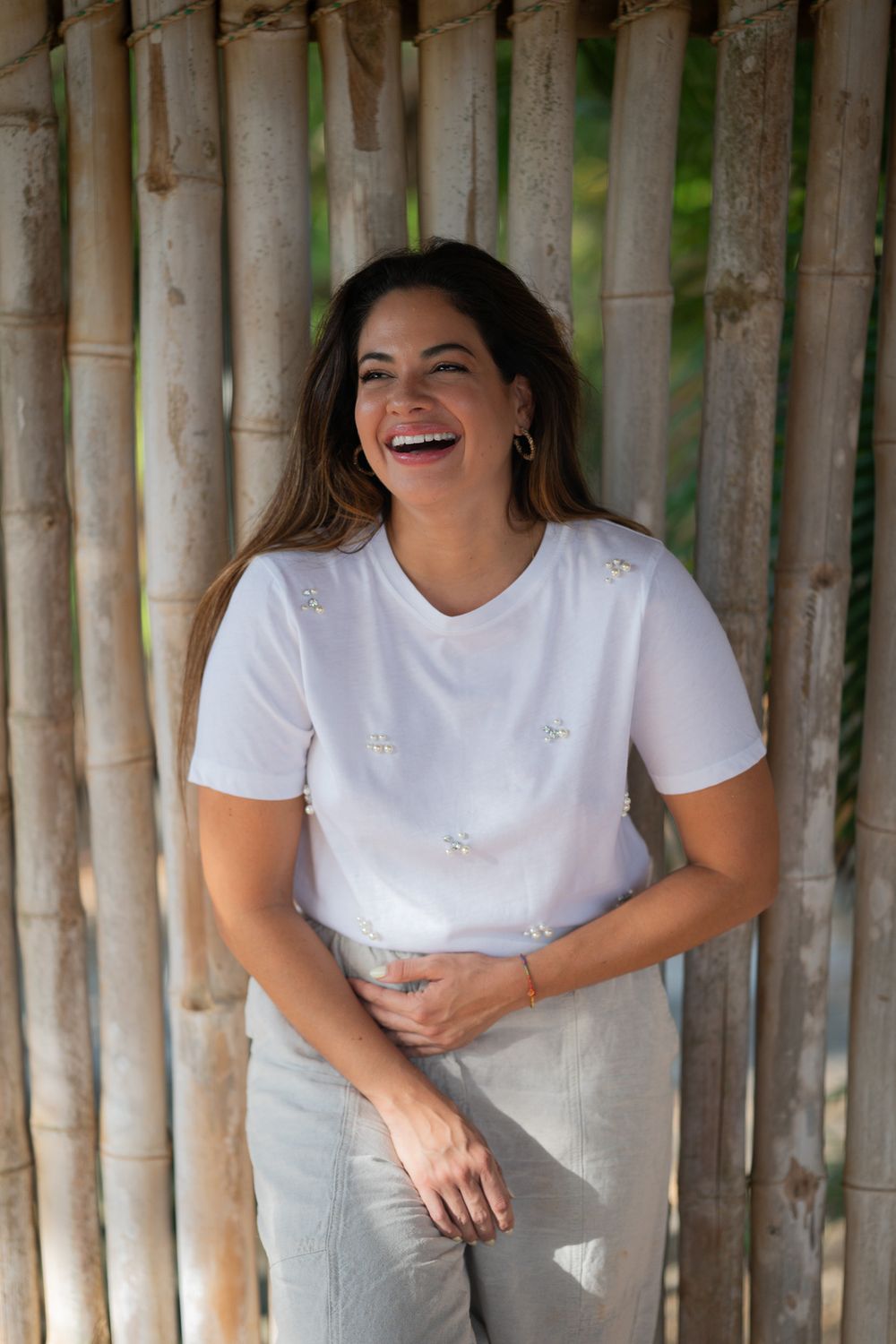 A person laughing joyfully against a bamboo wall backdrop wearing a white t-shirt.