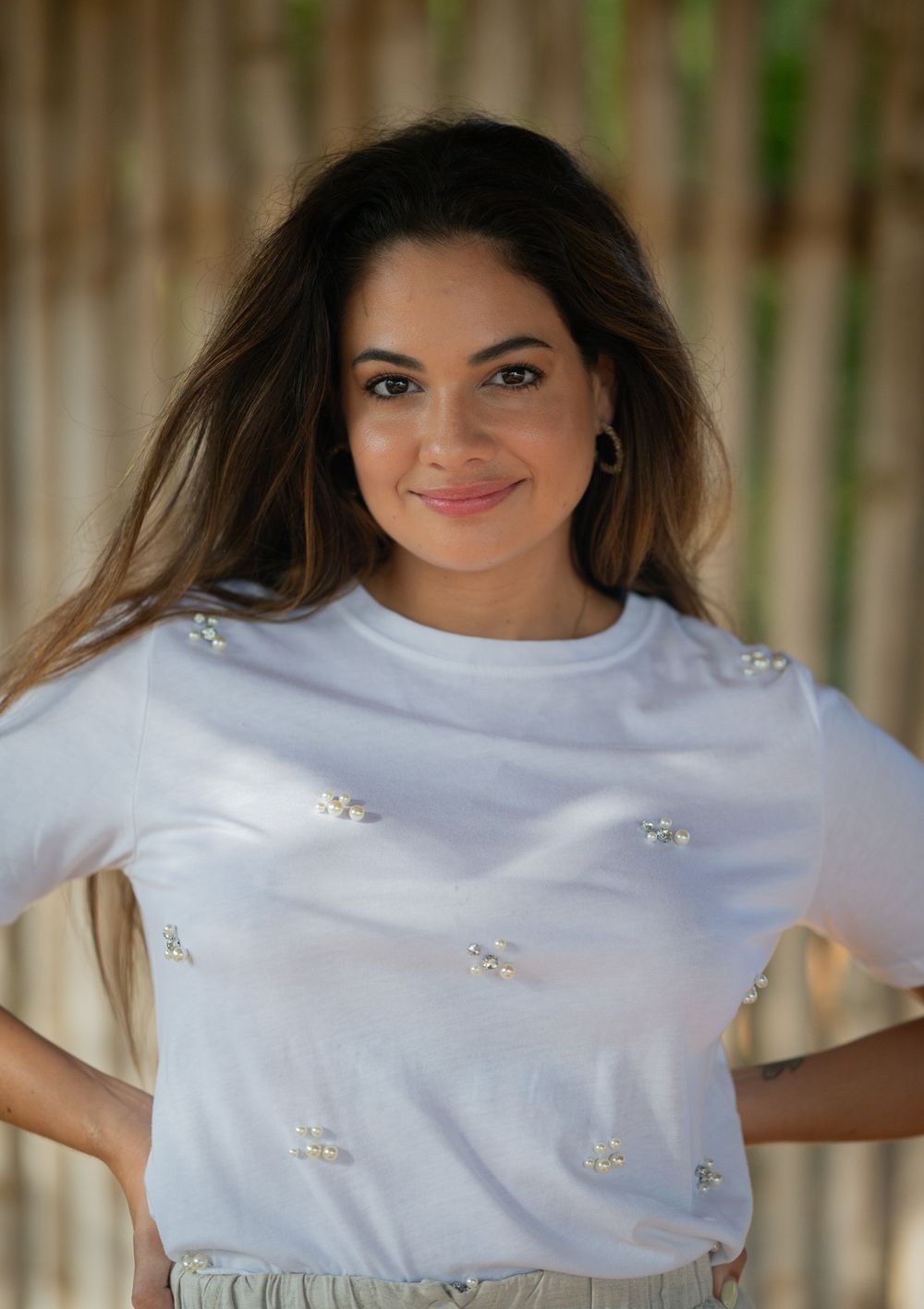 Woman in an embellished white t-shirt poses with hands on hips, showcasing casual elegant style.