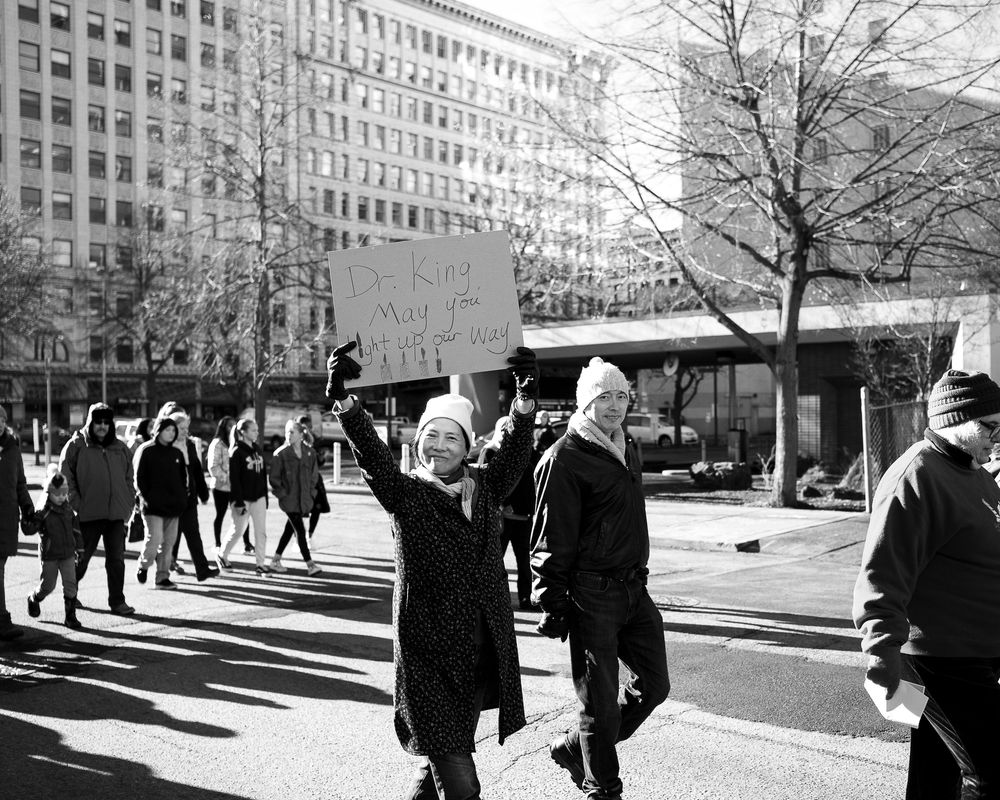 Black and white photo of protesters marching on a city street with signs and buildings in the background.
