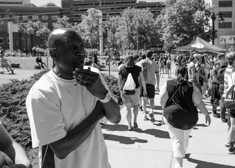 Black and white photo of a crowd gathering outdoors with someone speaking into a phone in the foreground.