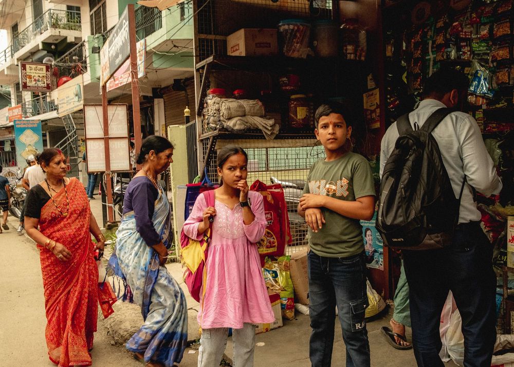 Busy street scene outside shops in an Indian marketplace with colorfully dressed people.
