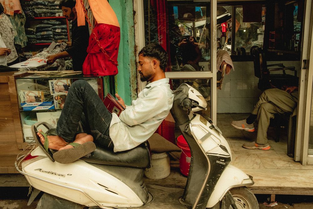 Two riders on a white scooter parked outside a storefront.