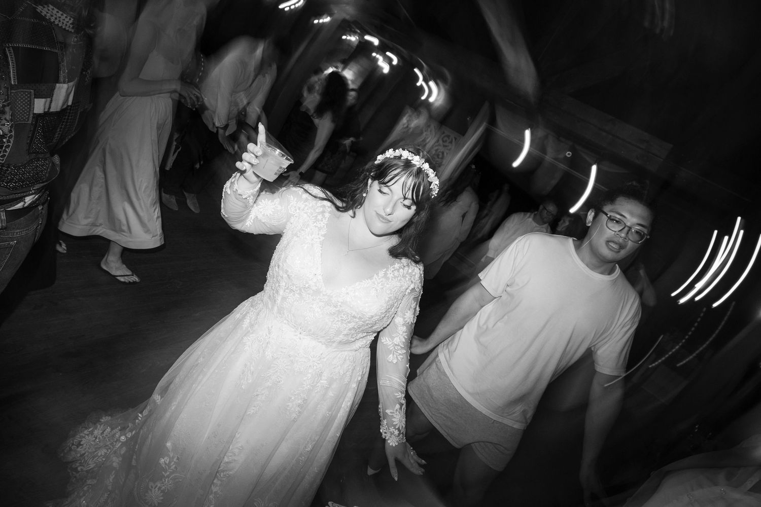 Black and white photo of guests dancing and moving on a dance floor at a wedding reception with motion blur effects.
