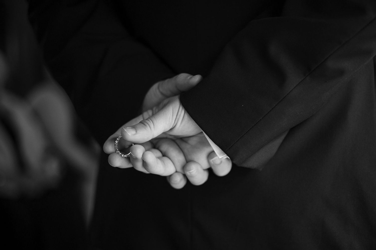A black and white close-up photograph of hands holding each other against a dark background.