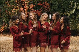 A group in burgundy outfits celebrates with wine glasses outdoors among autumn foliage and greenery.