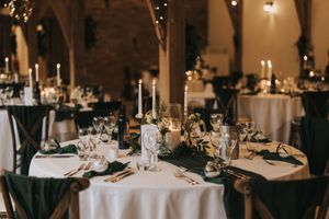 Elegant wedding reception table setting with white linens, candles and crystal glassware in a dimly lit venue.