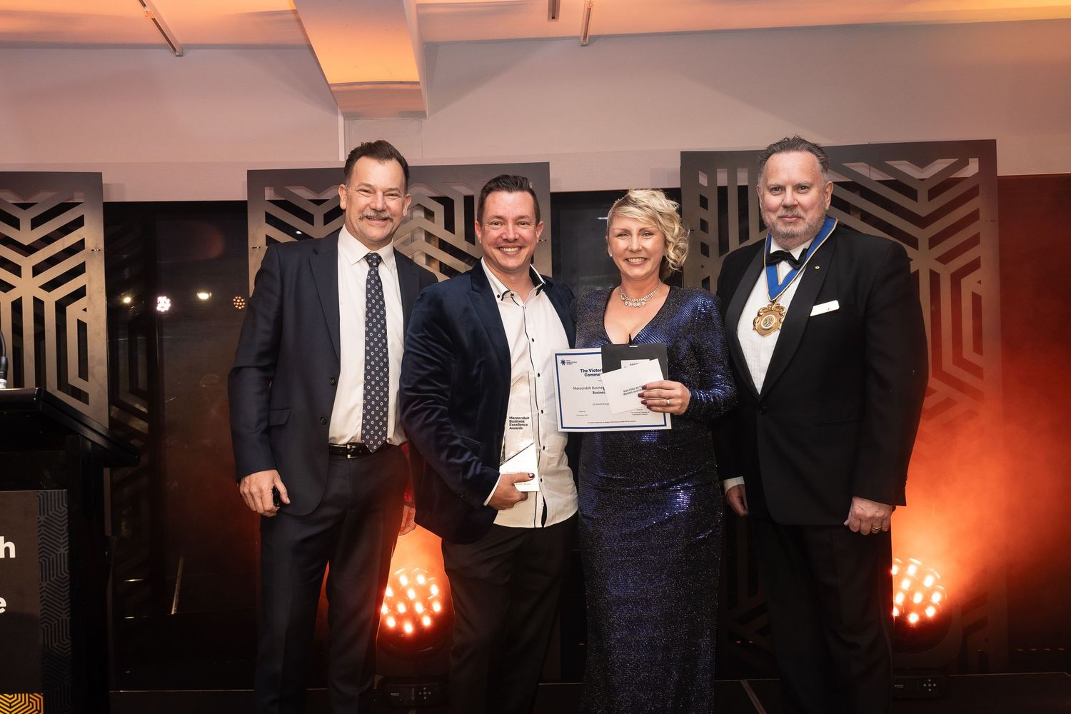 Four professionals pose together at an awards ceremony, with a woman holding a certificate and a man wearing a gold medal.