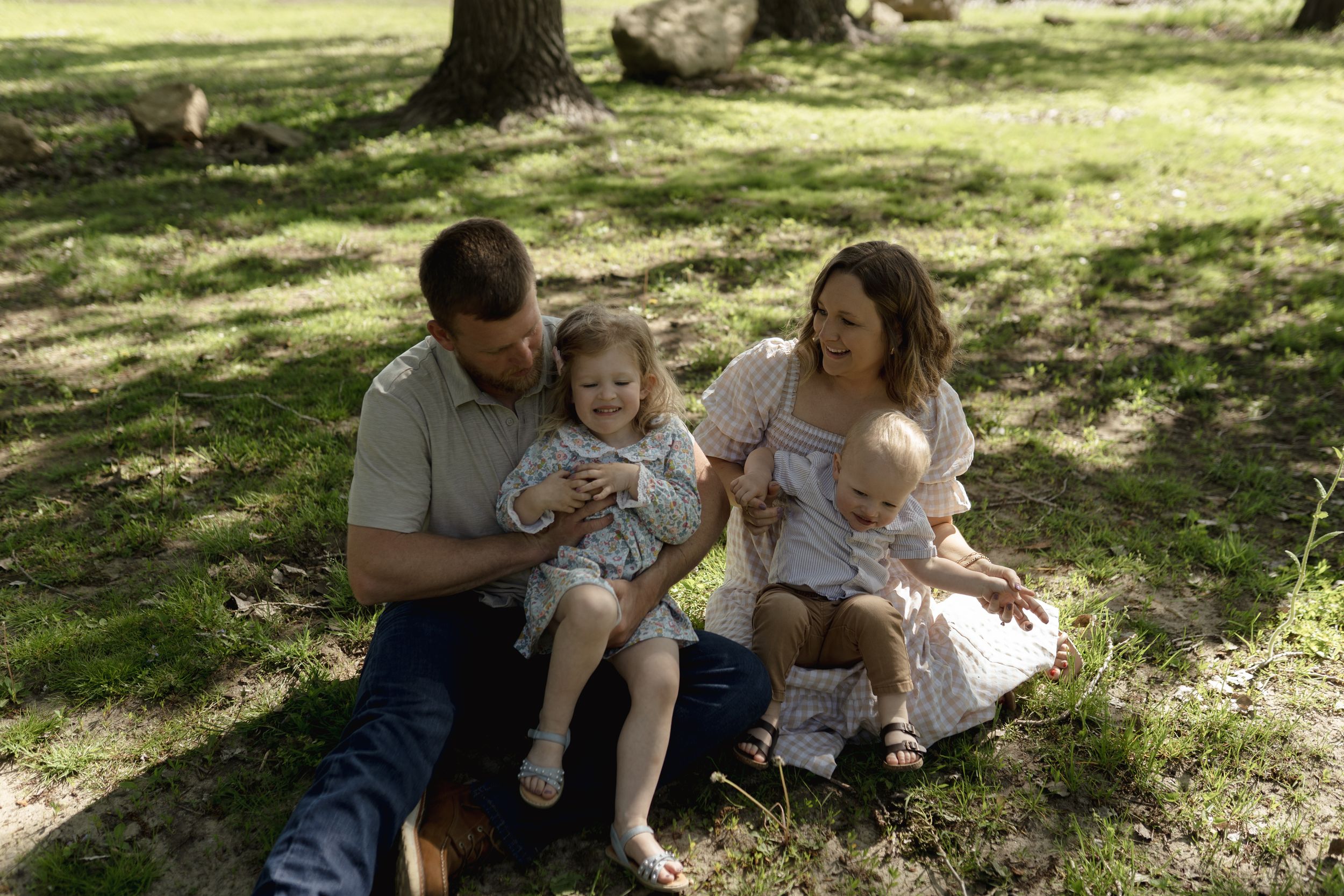 Family bonding moment captured under trees in sunlit park.
