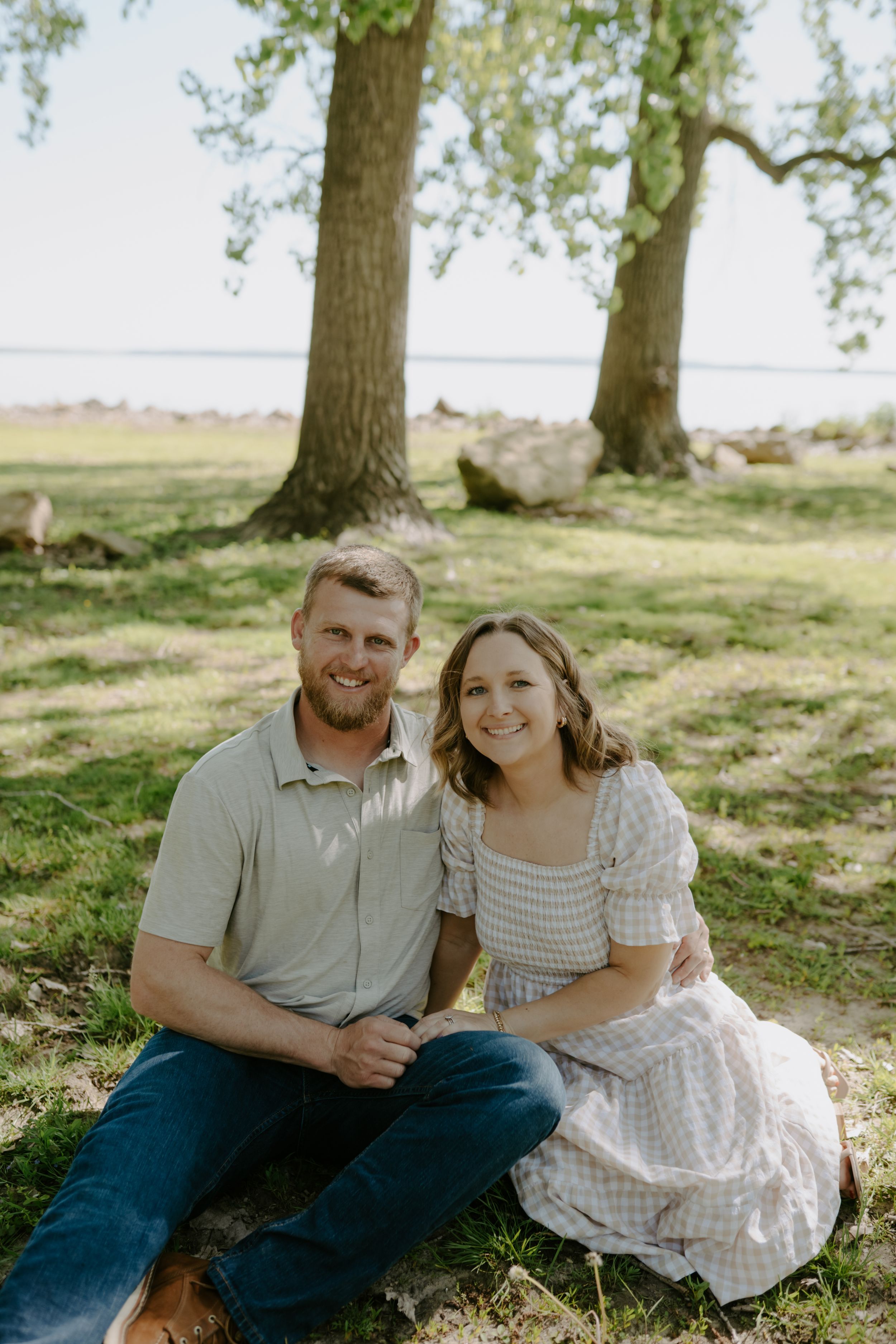 Couple sitting together under trees on a sunny day in a romantic outdoor setting.