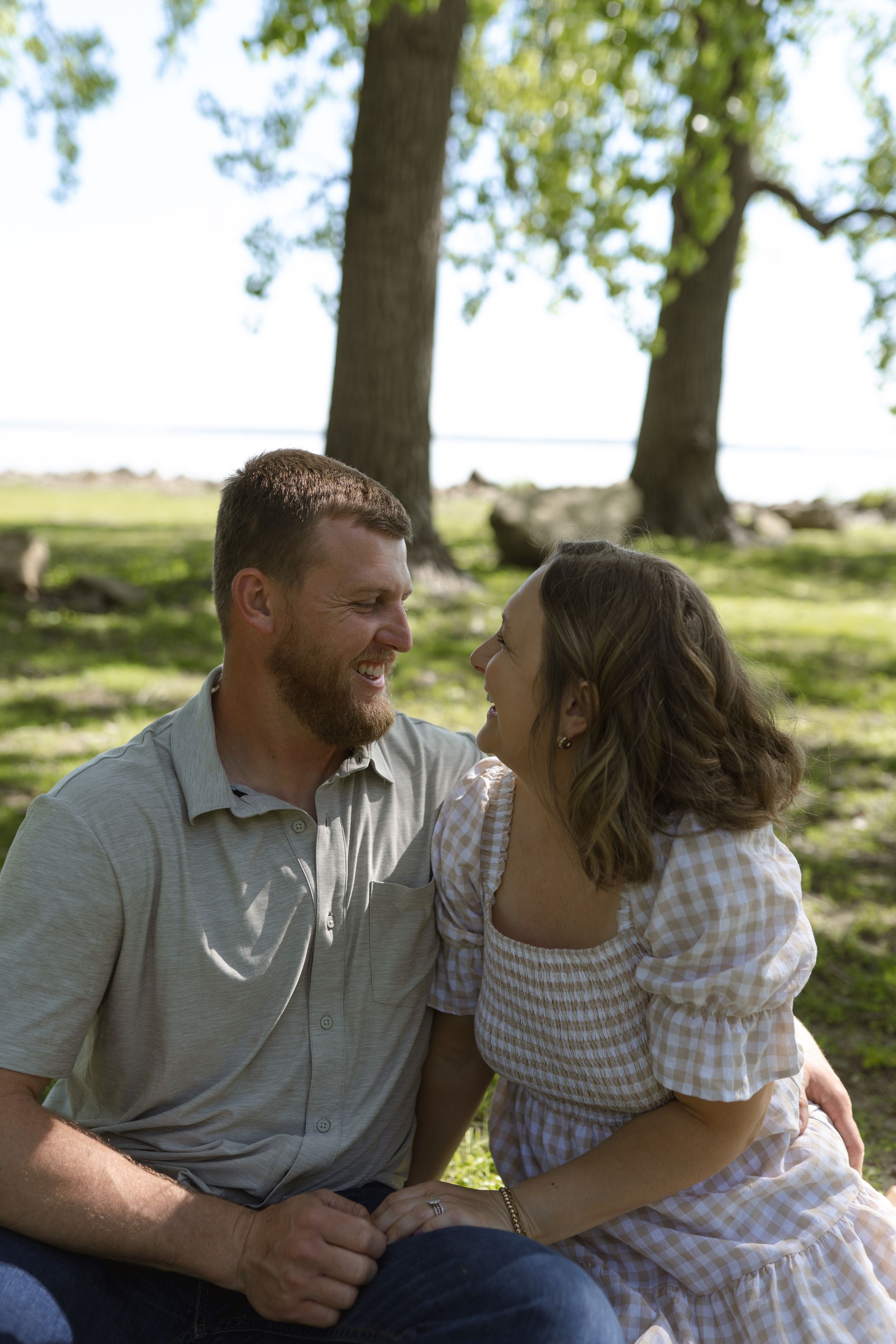 Candid outdoor portrait of a couple sharing laughter under a canopy of trees.
