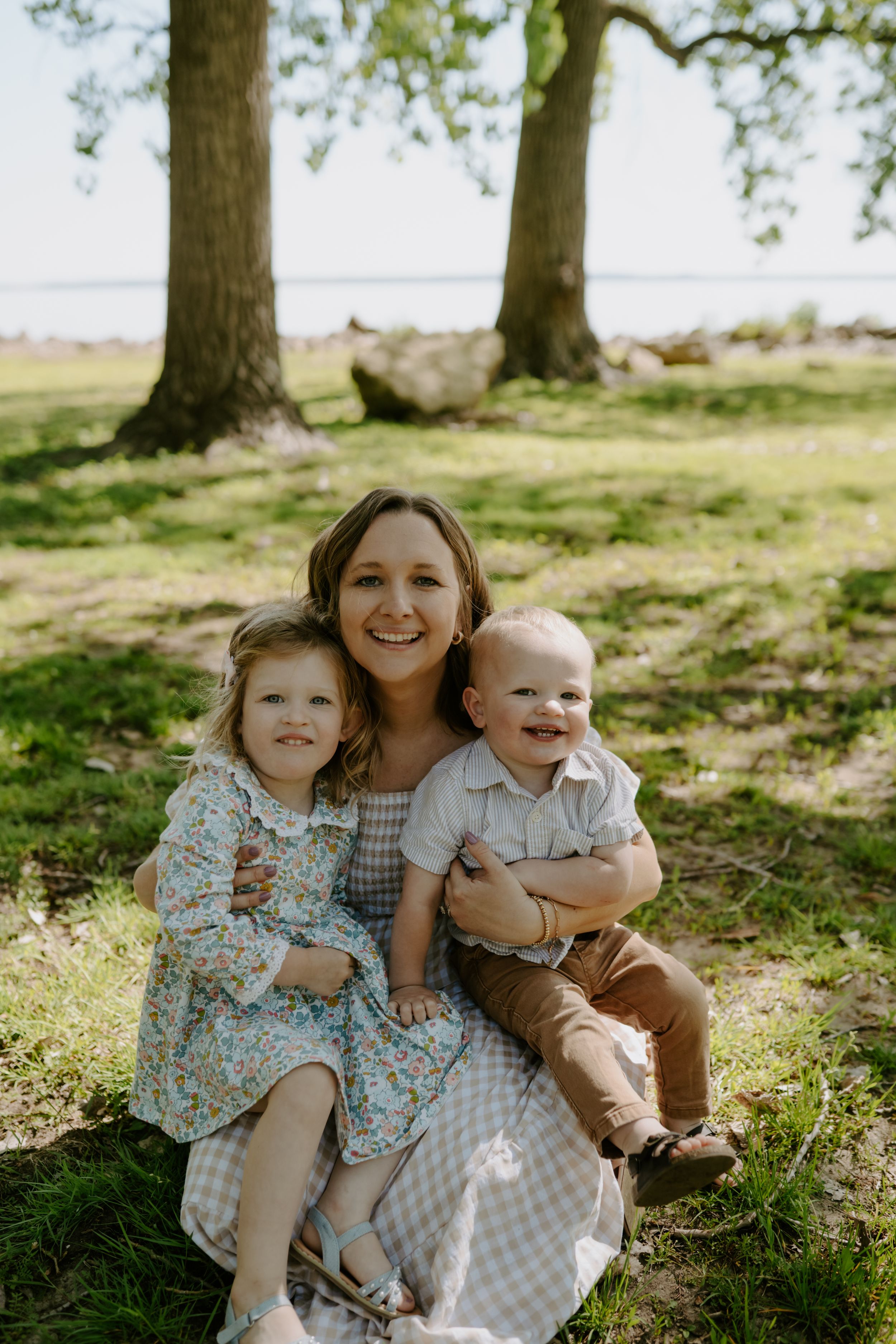 Family portrait in dappled sunlight showing joyful expressions and coordinated outfits.