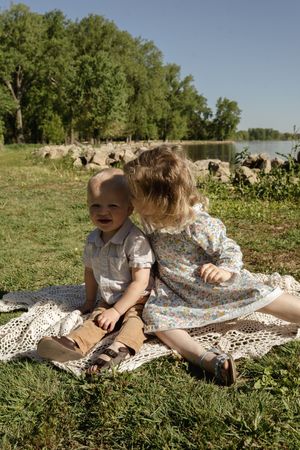 Children relaxing on a white lace blanket in a sunny meadow.
