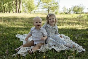 Playful outdoor photo session with children on decorative white blanket.