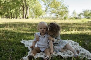 Candid family moment captured in natural sunlight on white lace blanket.