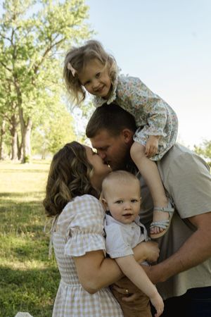 Playful family embracing and laughing together in a sunny park setting.
