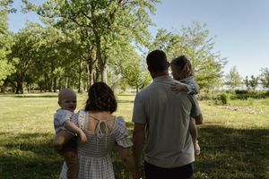 Silhouettes of a family embracing against a bright outdoor background with trees.