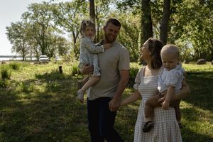 Family portrait session in a lush green park with dappled sunlight filtering through trees.