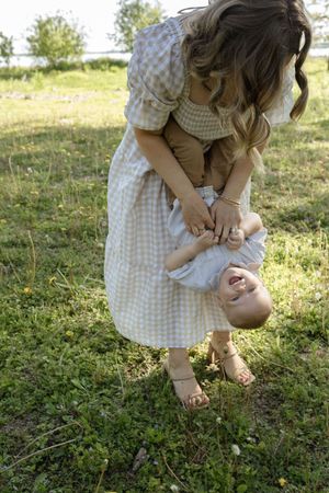 A playful moment in a sunny field as a gingham dress-clad figure holds a small child upside down.