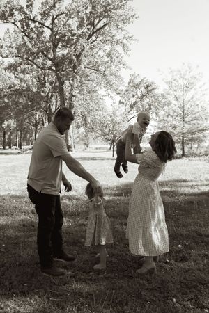 A black and white photo of a family playing together under trees in a park.