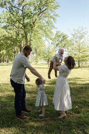A joyful family moment captured in a sunlit park with tall trees in the background.