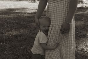 A tender black and white image showing a small child hugging a gingham dress in a park setting.