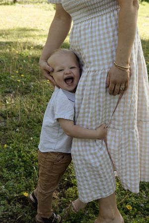 A joyful toddler laughs while holding onto a gingham dress in a sunny field.
