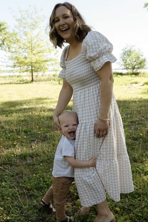 A heartwarming moment between two figures in a gingham dress and white shirt against a sunny backdrop.