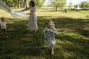 Family enjoying a playful moment with white fabric in a grassy park.