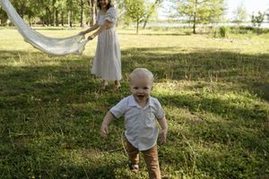 Small child running through a sunny park while others hold white fabric.