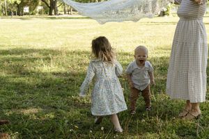 Children playing in a sunlit field with flowing fabric on a summer day.