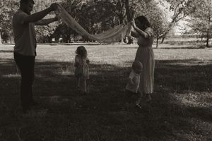 Black and white photo of family playing with fabric in a park setting.