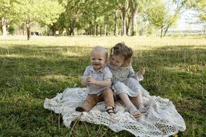 Two children sitting together on a white lace blanket in a park.
