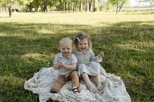 Children sharing a sweet moment while sitting on decorative lace in a park.