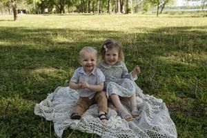 Two children laughing together on white lace blanket outdoors.
