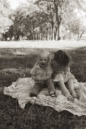 Black and white portrait of children sharing joyful moment on lace blanket.
