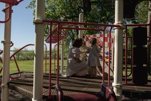 Children playing together on red metal playground equipment in a sunny outdoor setting.