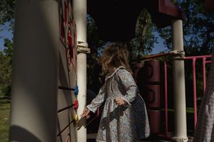 Child in a floral dress exploring playground equipment in natural lighting.
