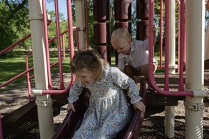 Children playing on red and white playground equipment in dappled sunlight.