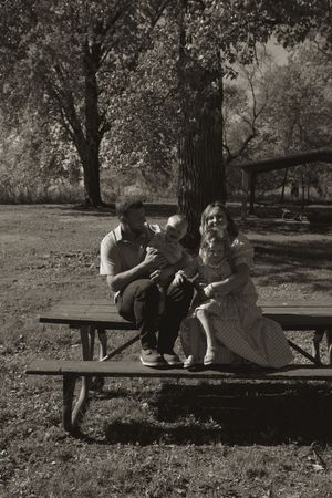 A black and white photo of people relaxing on a park bench surrounded by trees.
