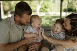 An intimate family scene unfolds on a park bench during a sunny afternoon.