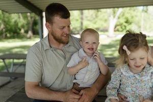A loving family embraces while sitting together on a wooden bench under a shelter.